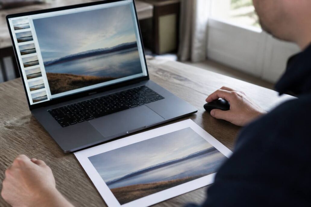 Close-up van het controleren van foto’s op een laptop en een printproef op tafel